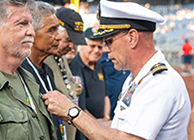 Navy Commander in white uniform puts a Vietnam Veterans Lapel Pin on a Vietnam Veteran at Nationals Park
